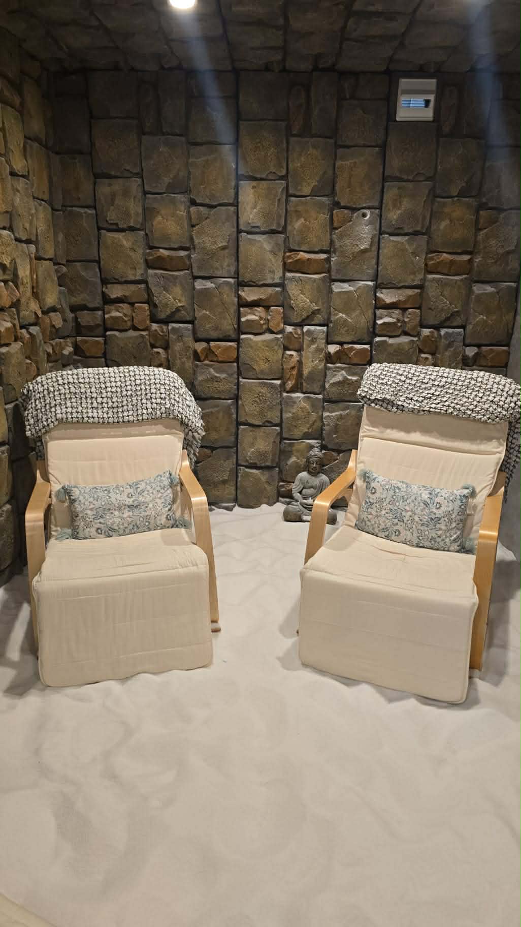 Two lounge chairs on a white salt floor against a rustic stone-textured wall.