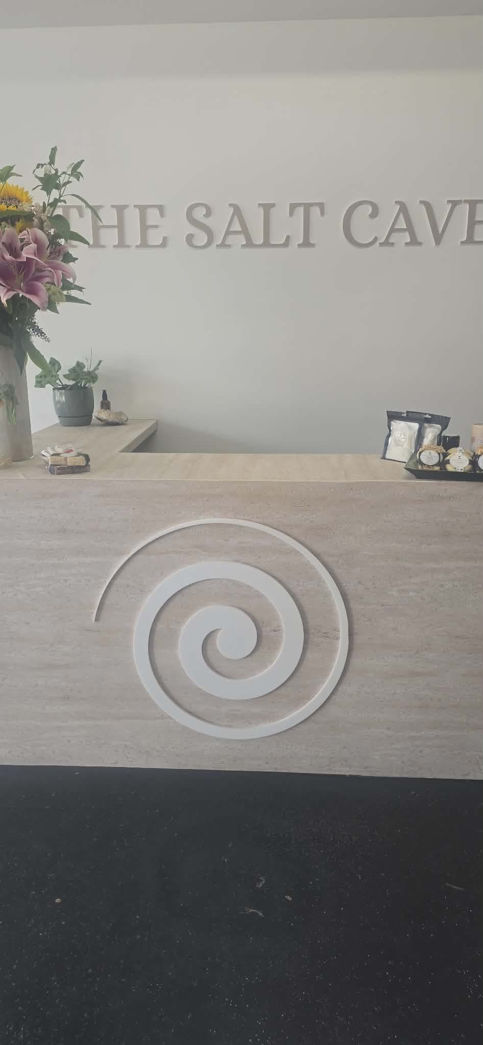 Reception desk at The Salt Cave with a white spiral logo and floral arrangement.